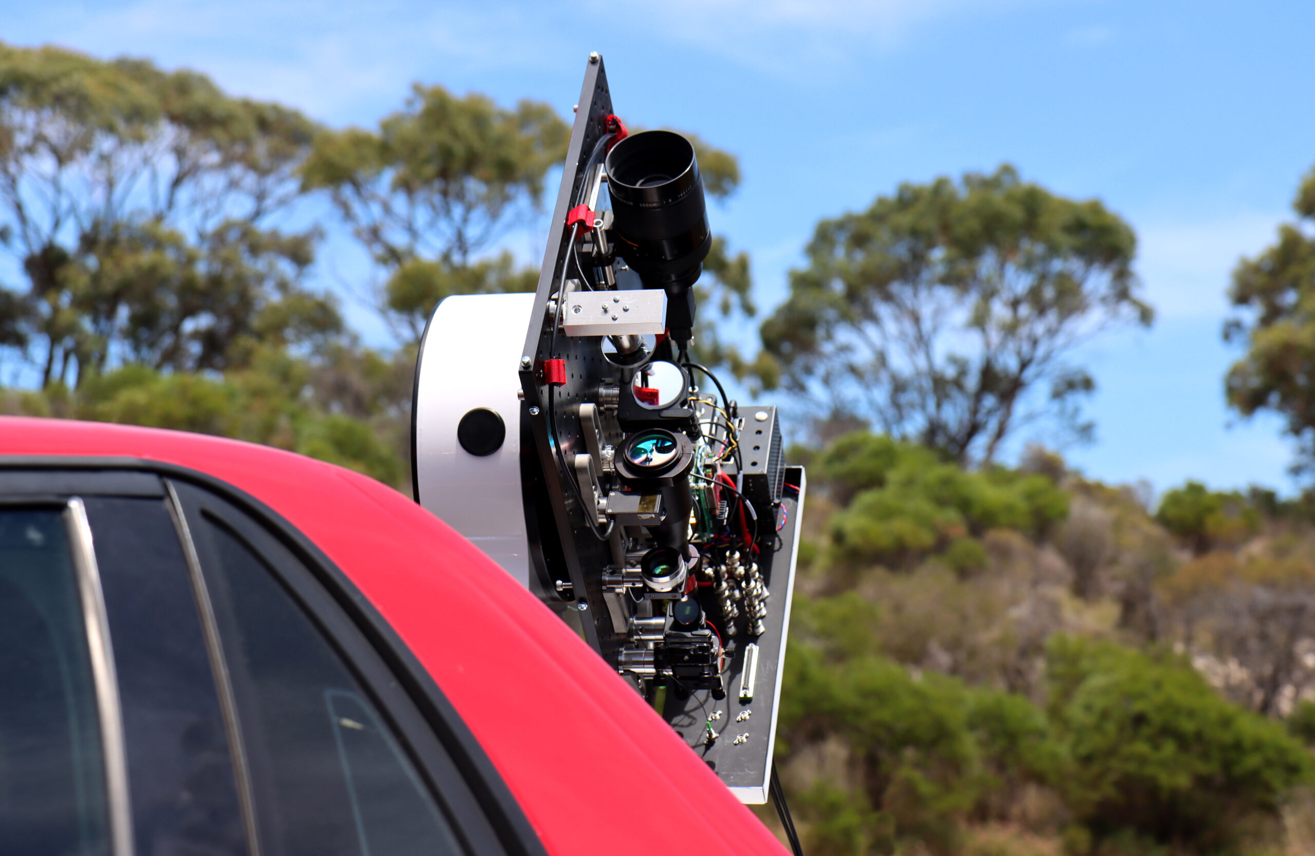 An assembly of lenses, mirrors and lasers are mounted on a board and pointed at the sky.